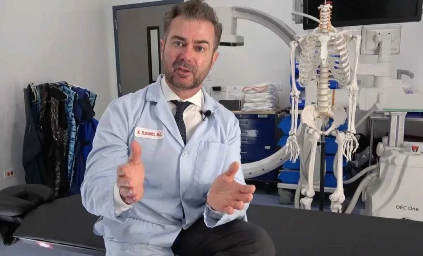 Dr. Elbaridi speaking in a procedure room beside a skeleton model