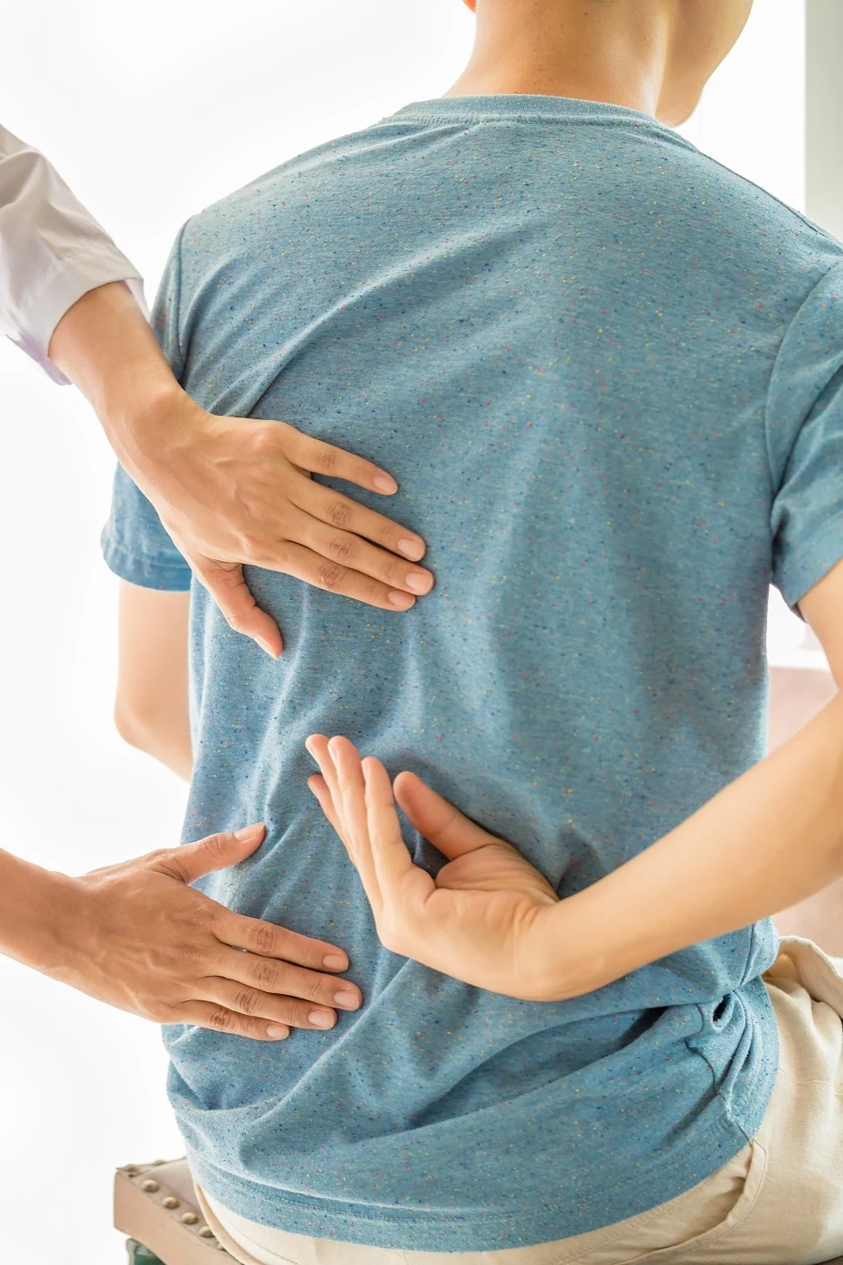 Clinician’s hands examining a man’s lower back