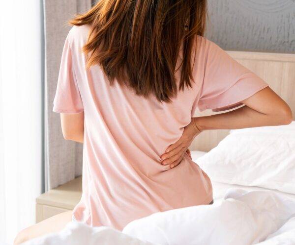 Back view of young Asian woman suffering from backache on bed in the morning. close up