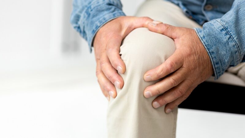 Senior man suffering from knee pain. Close up of mature male massaging his painful knee while sitting on sofa at home
