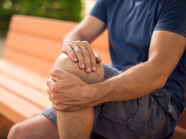 Man with knee pain sitting on the bench in the park. Healthcare and medicine concept